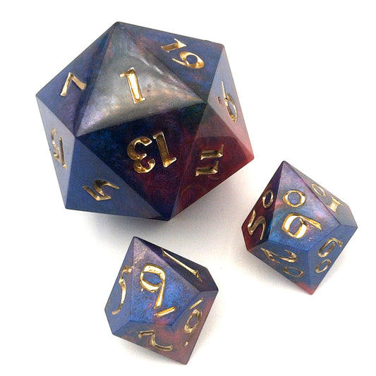 Full set of Mothership dice. The D20 is a chonk, and the D10 and D100 are regular size. The resin is coloured with pigment powders using black, blue and red. The dice are inked in chromed gold.