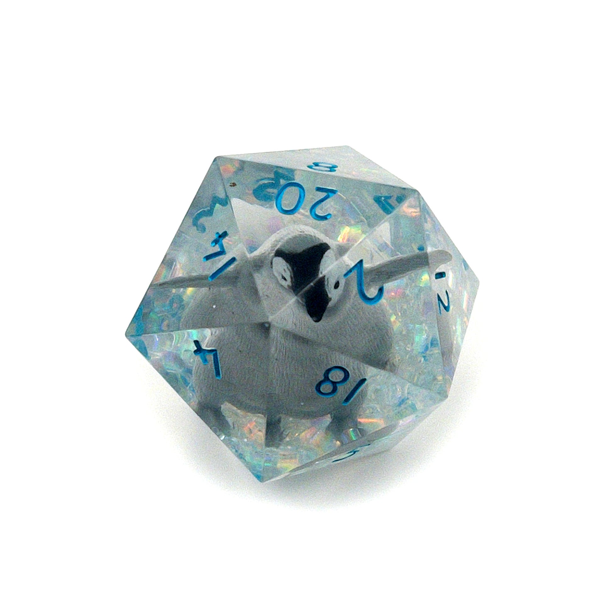 Clear resin D20 chonk showing the 20 face, with a toy penguin inside. The chonk has iridescent mylar tubes and glitter at the bottom, and is inked in ice blue