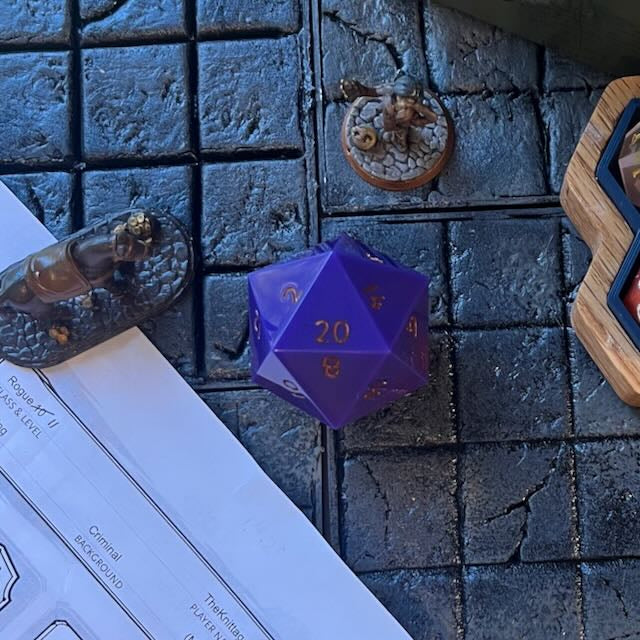 Purple through red opaque pearlescent minimalist D20 chonk with gold inking on the numbers on a D&D table