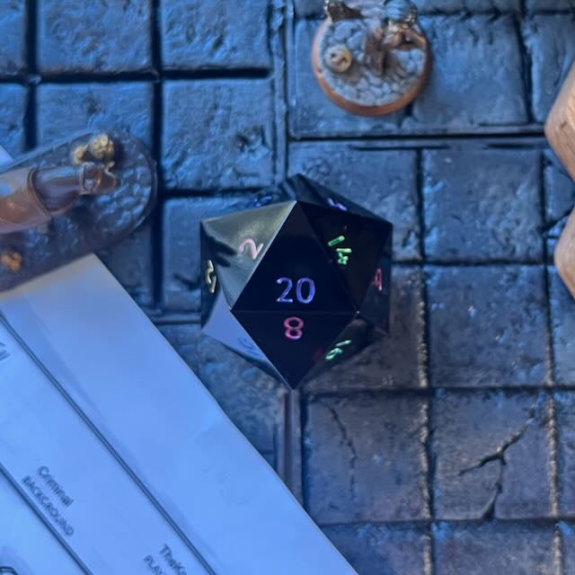 Minimal Black Opaque D20 Chonk with multiple colours used for inking numbers on a D&D table