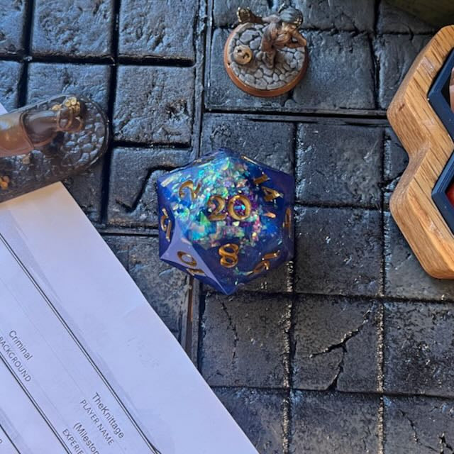 Blue opaque D20 chonk with large glitter flakes on a D&D table