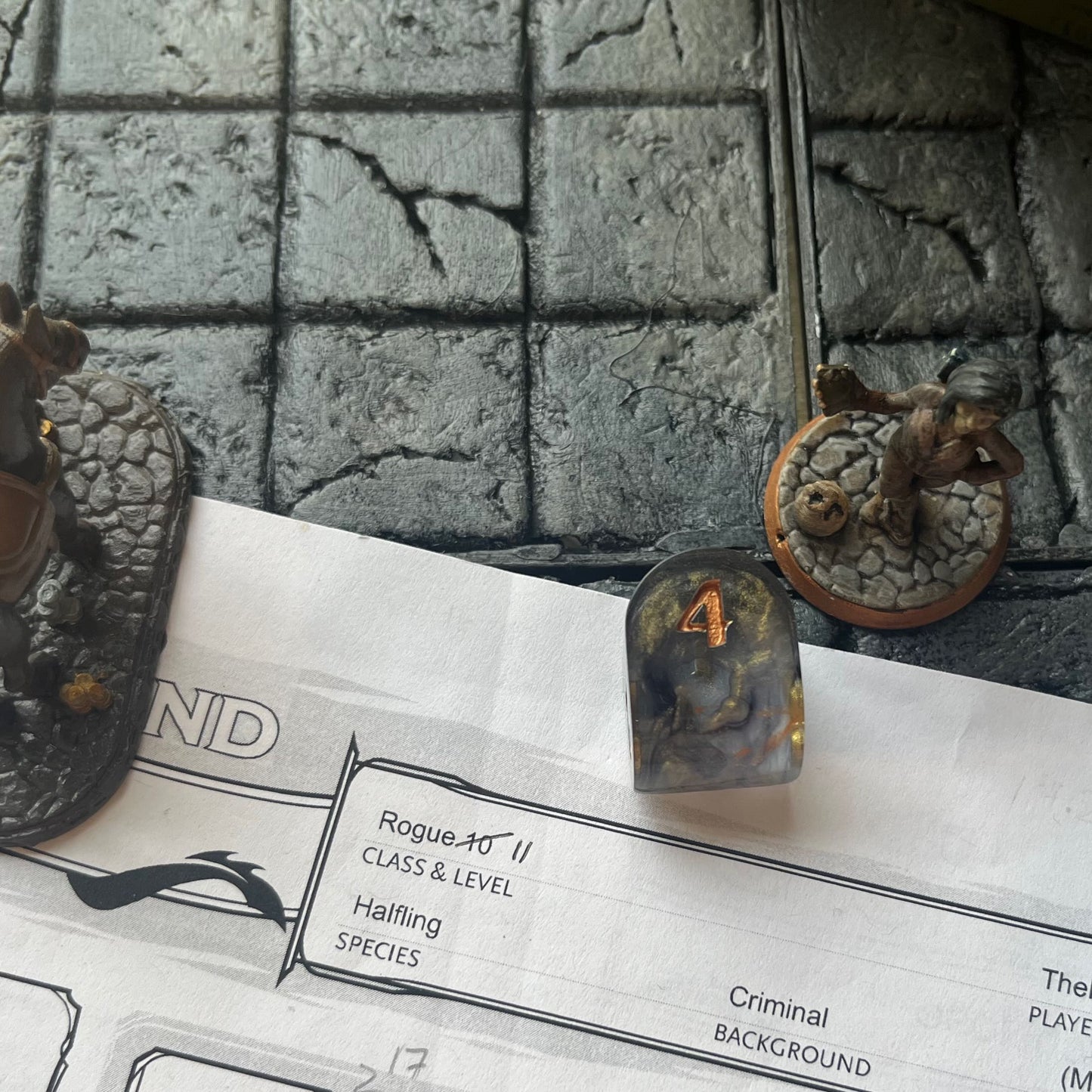 Resin infinity-shaped D4, semi-transparent using black and gold swirled dyes and inked in gold on a D&D background
