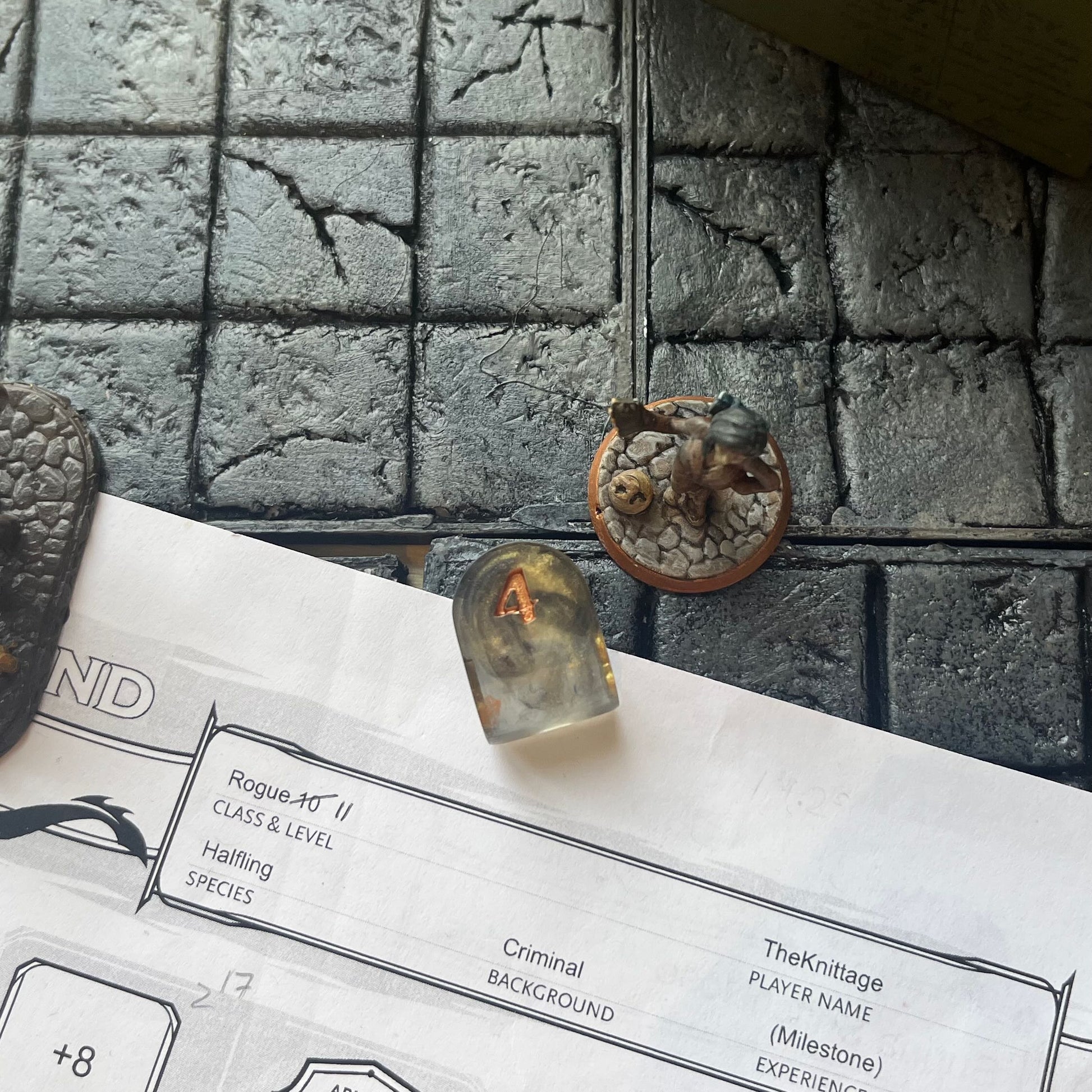 Resin infinity-shaped D4, semi-transparent using black and gold swirled dyes and inked in gold on a D&D background