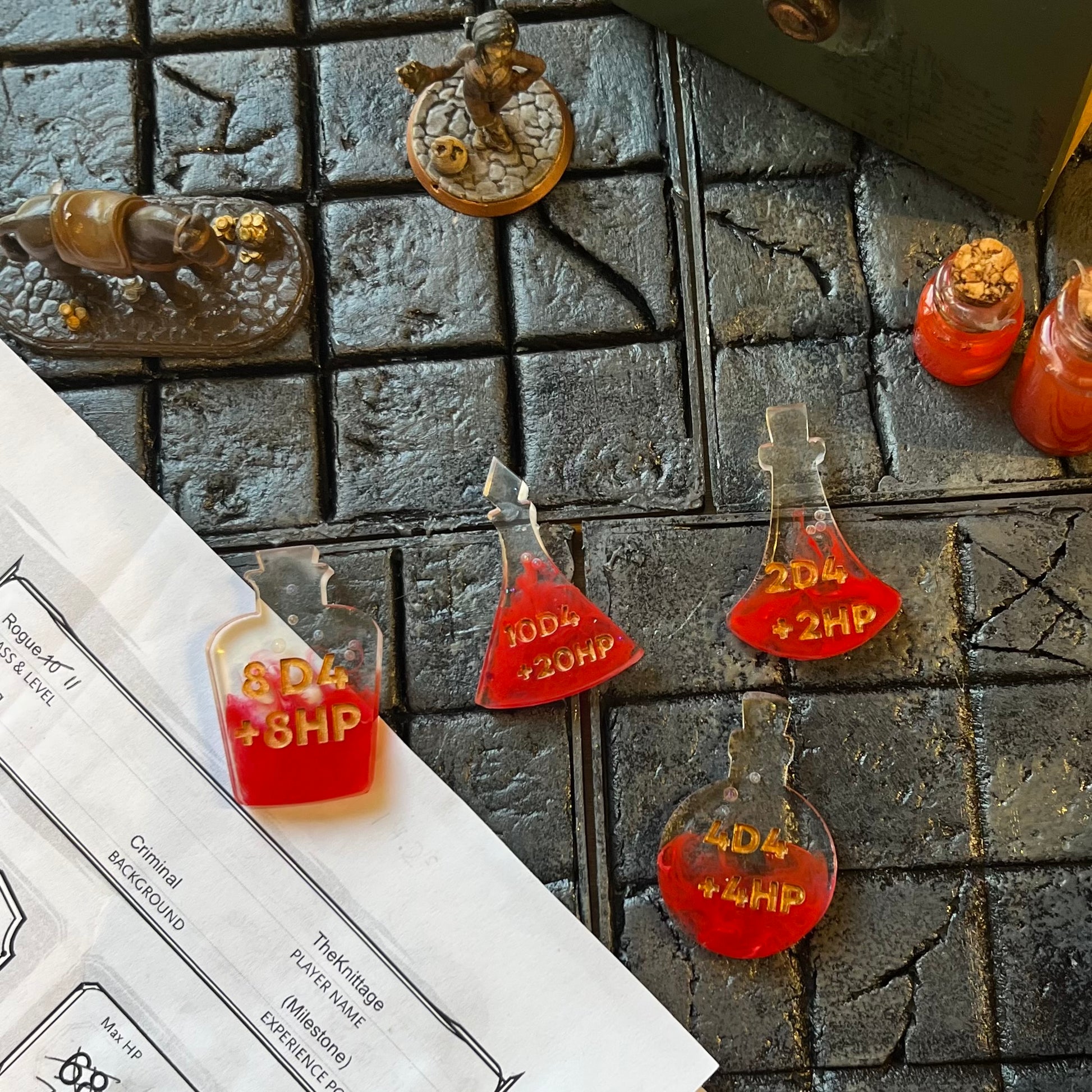Resin potion bottles with red alcohol ink colouring and gold lettering shown on a D&D play table