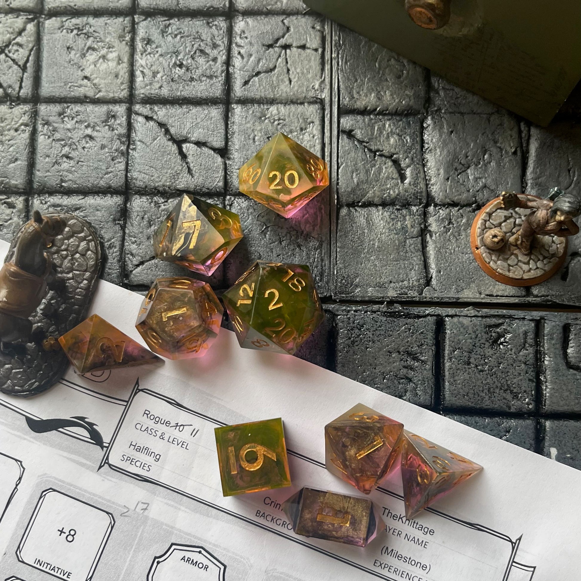 Full set of TTRPG resin dice shown on a D&D background. Resin is semi-transparent pigmented with gold, black and amber dyes. These are inked in gold