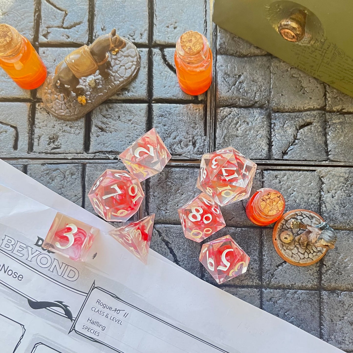 Full set of TTRPG dice. Transparent resin with a swirl of red dyed resin through the centre, known as 'Blood in the Water'. Inked in white. Shown on a D&D background