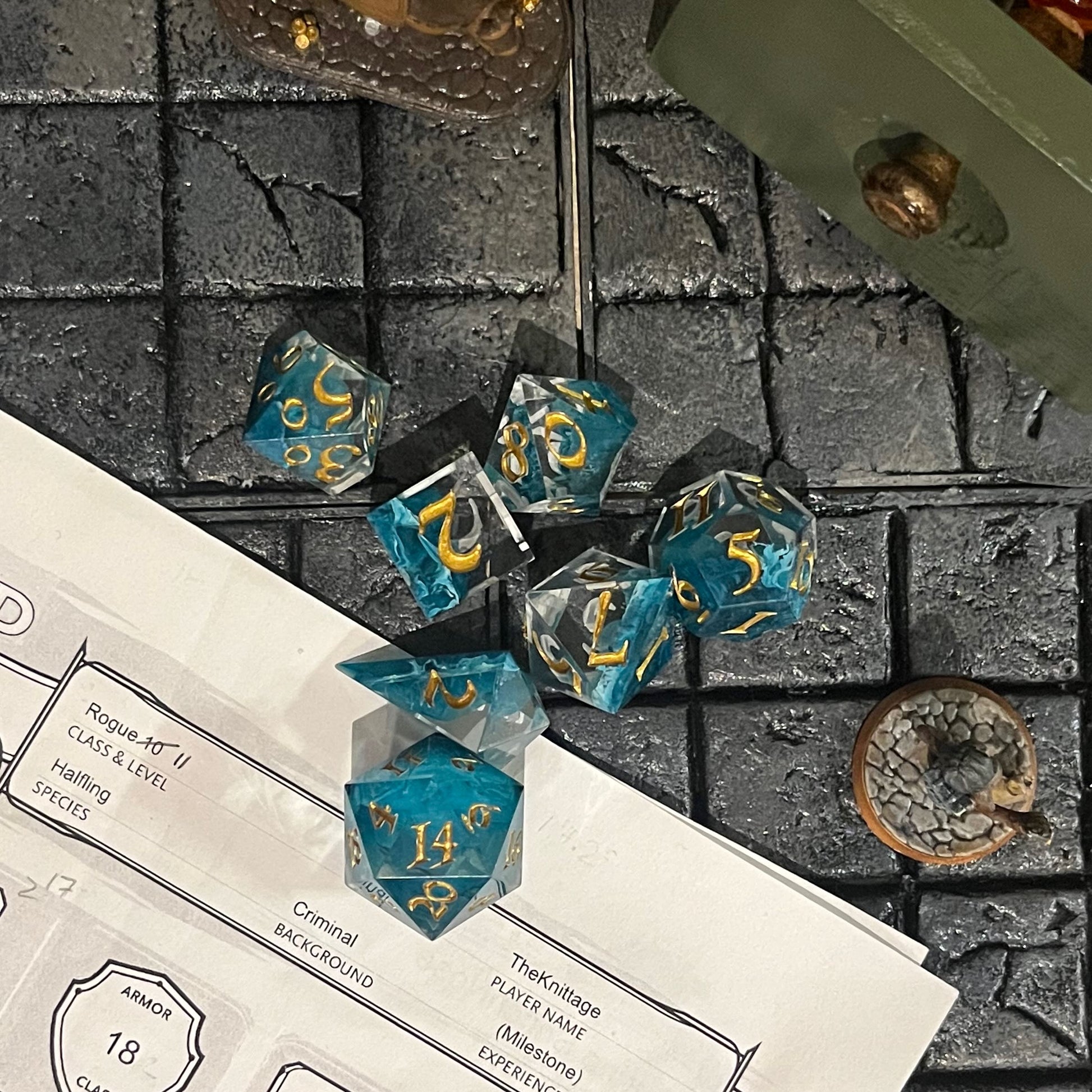 Full set of TTRPG resin dice, petri-pour in white and Smurf blue, inked in Gold on a D&D background