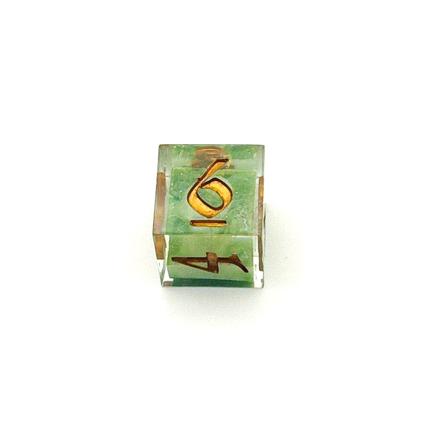 D6 TTRPG resin die, with green and white pigment cast into blanks and then shelled in clear resin and inked in Chromed Gold