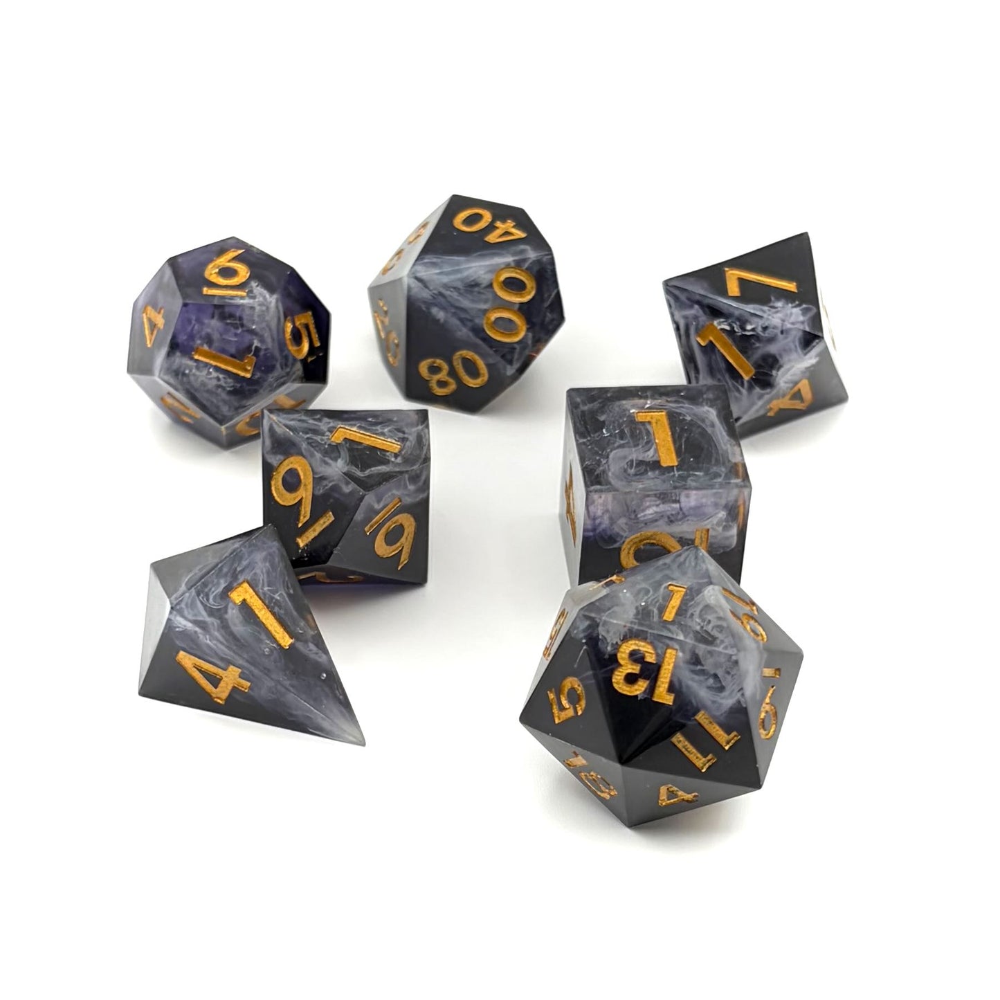 Photo showing a set of 7 resin TTRPG dice. Opaque black with wisps of white. Inking is gold