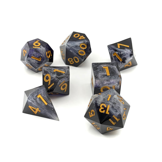 Photo showing a set of 7 resin TTRPG dice. Opaque black with wisps of white. Inking is gold