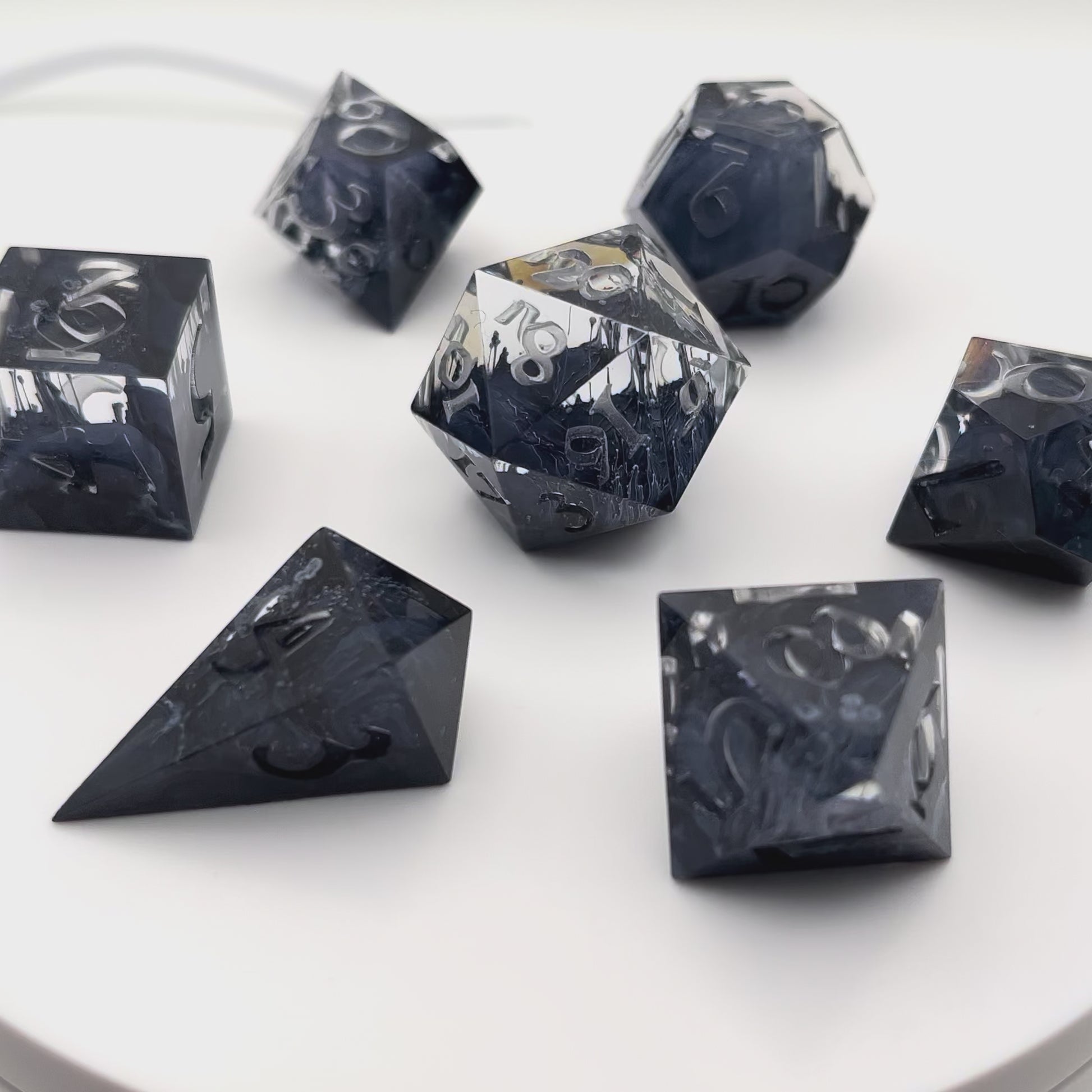 Video showing a full set of clear and black petrie pour style resin dice rotating in a lightbox. Uninked numbers