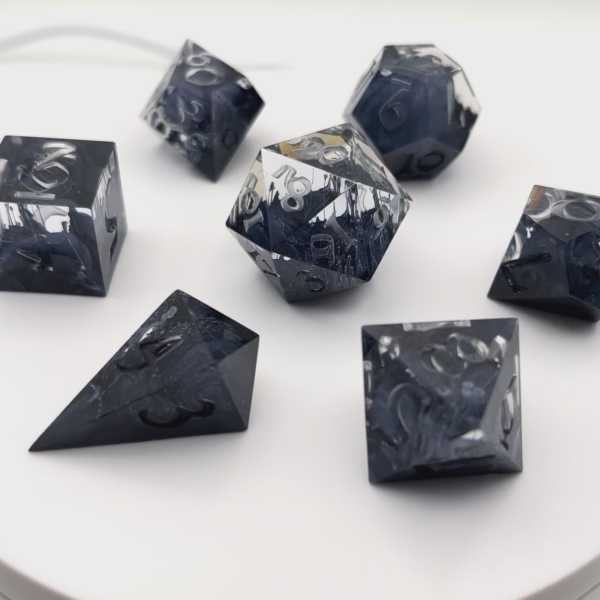 Video showing a full set of clear and black petrie pour style resin dice rotating in a lightbox. Uninked numbers