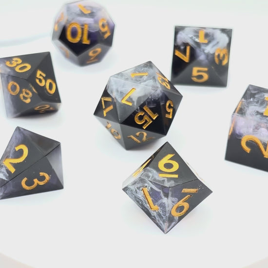 Video showing a set of 7 resin TTRPG dice. Opaque black with wisps of white. Inking is gold