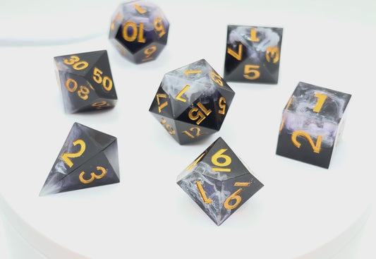 Video showing a set of 7 resin TTRPG dice. Opaque black with wisps of white. Inking is gold