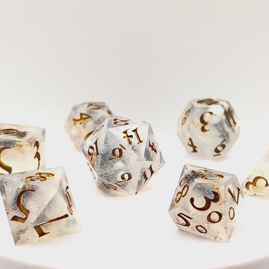 Video of Full set of TTRPG dice, semi-transparent resin with translucent glitter and angel wing and pearl beads suspended inside. Inked in gold