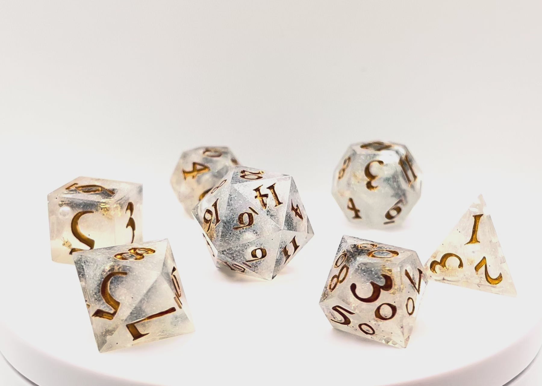 Video of Full set of TTRPG dice, semi-transparent resin with translucent glitter and angel wing and pearl beads suspended inside. Inked in gold