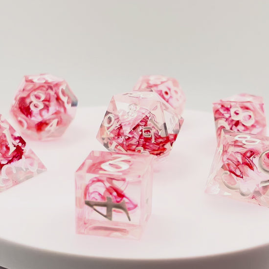 Video showing Full set of TTRPG dice. Transparent resin with a swirl of red dyed resin through the centre, known as 'Blood in the Water'. Inked in white