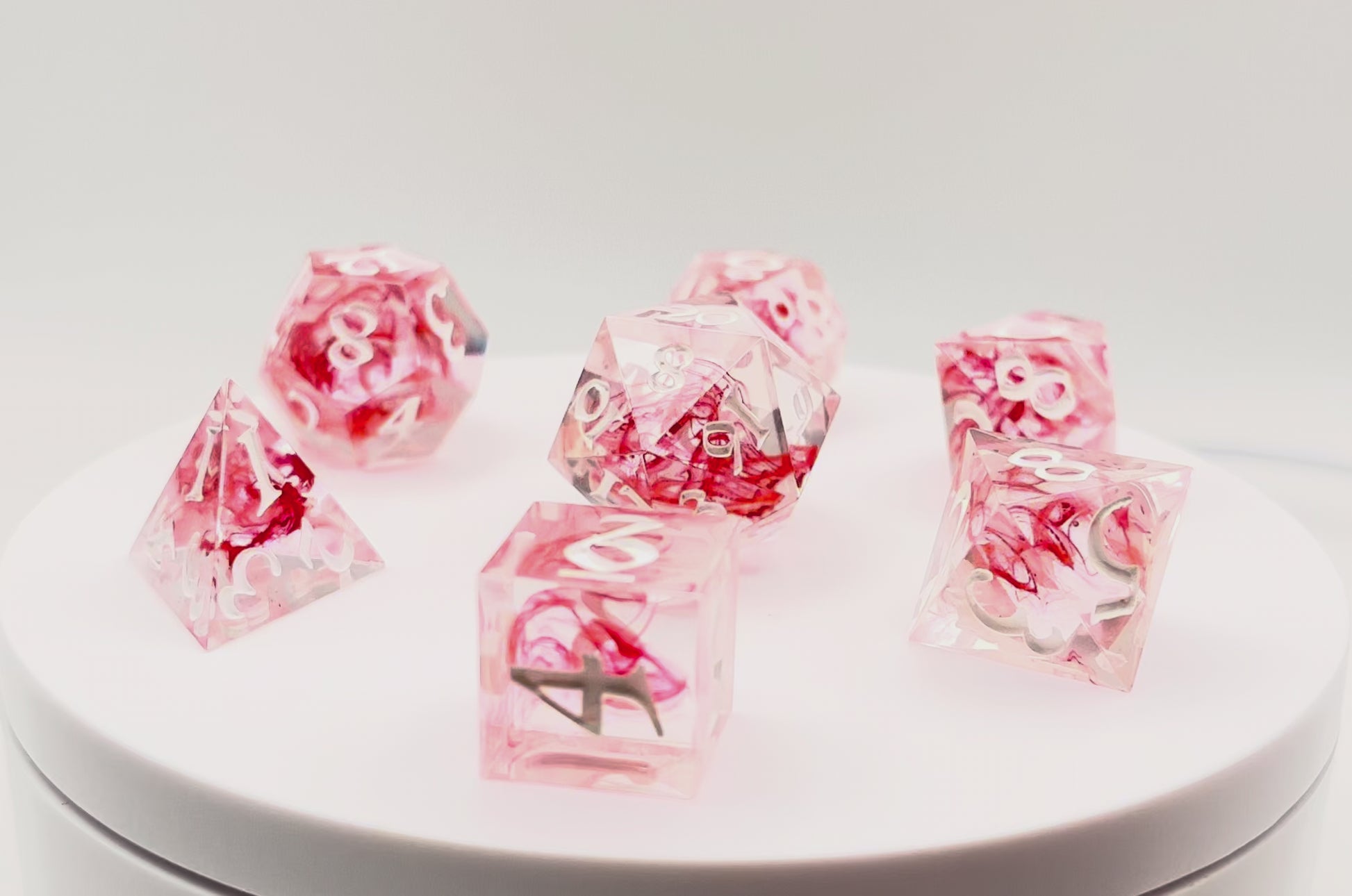 Video showing Full set of TTRPG dice. Transparent resin with a swirl of red dyed resin through the centre, known as 'Blood in the Water'. Inked in white