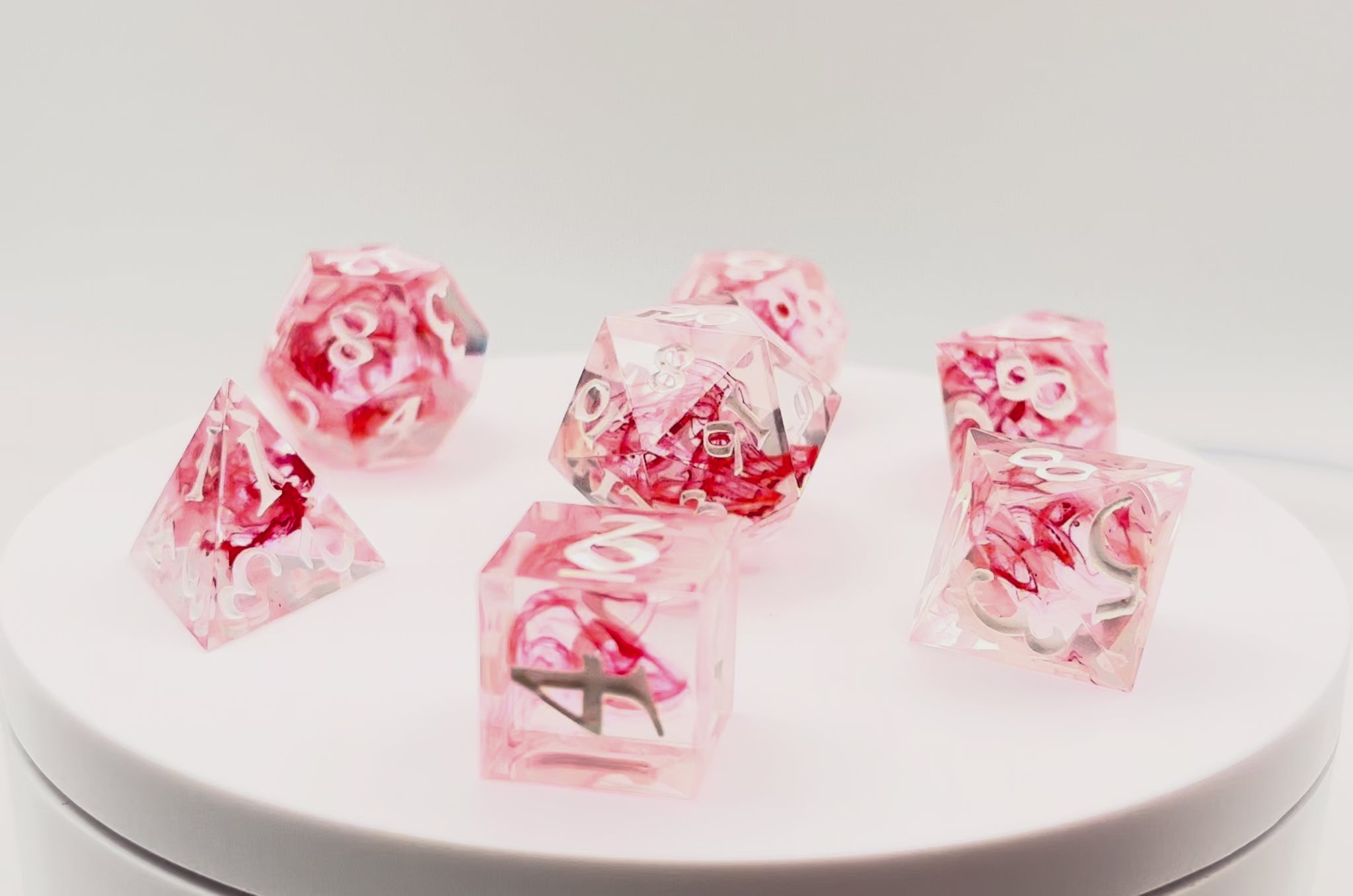 Video showing Full set of TTRPG dice. Transparent resin with a swirl of red dyed resin through the centre, known as 'Blood in the Water'. Inked in white
