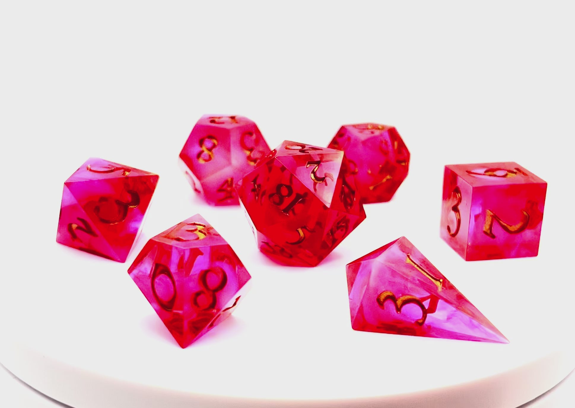 Video showing Full set of TTRPG semi-transparent resin dice, coloured with red and pink dye, with a soft blur of resin coloured with Piñata Blanco Blanco white in the centre and inked in gold
