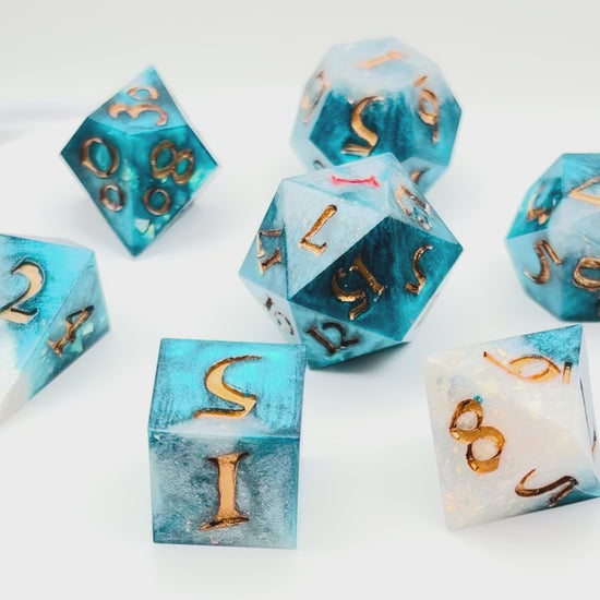 Video of 7 resin TTRPG dice. Rich teal and white opaque resin, with gold inking