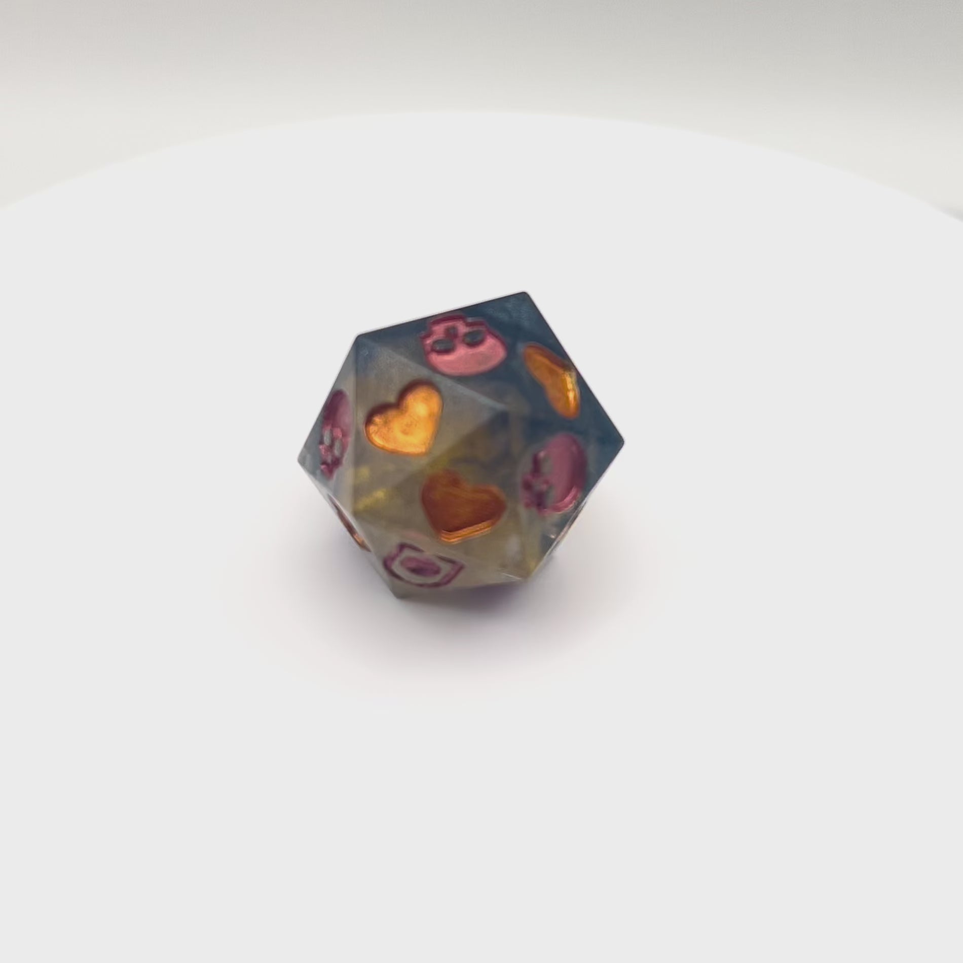 Video of resin D20 dice used for Death Saves in TTRPG. Semi transparent gold and black, skulls inked in copper and hearts inked in gold